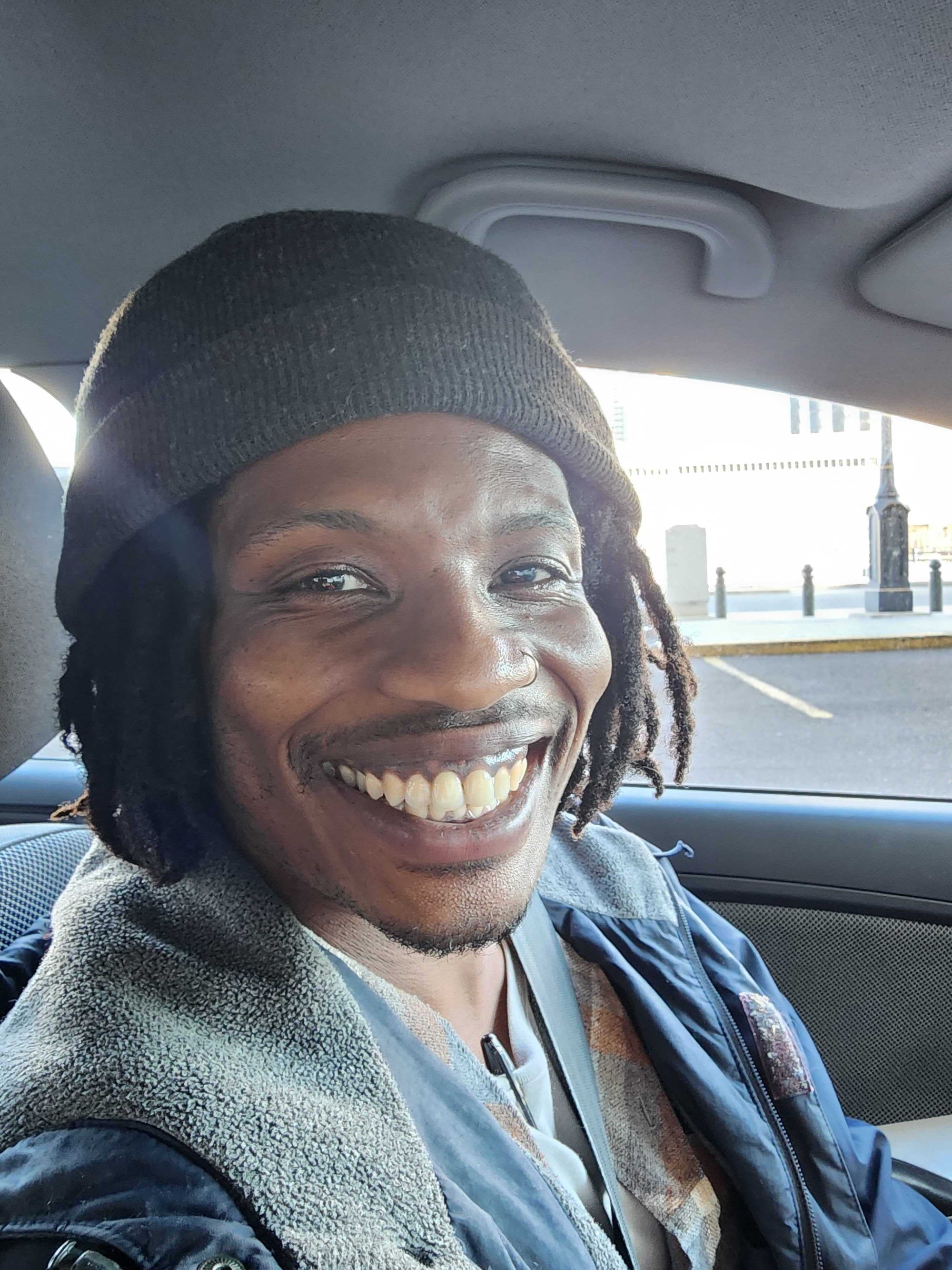 Ruben is sitting in a car, wearing a hat and smiling.