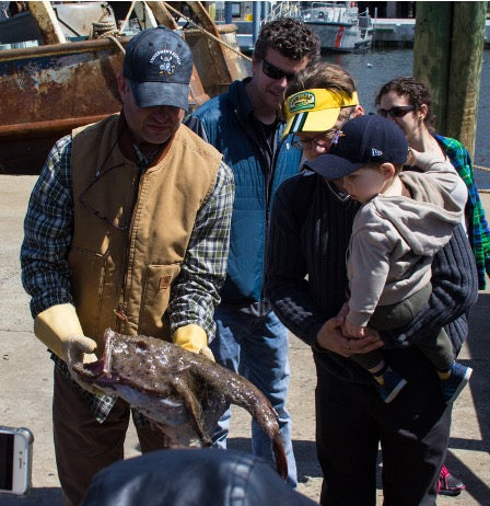 Dock manager Steve Bardsley showing a monkfish to Fishadelphia Seafood Club Member Michael Hodges and family