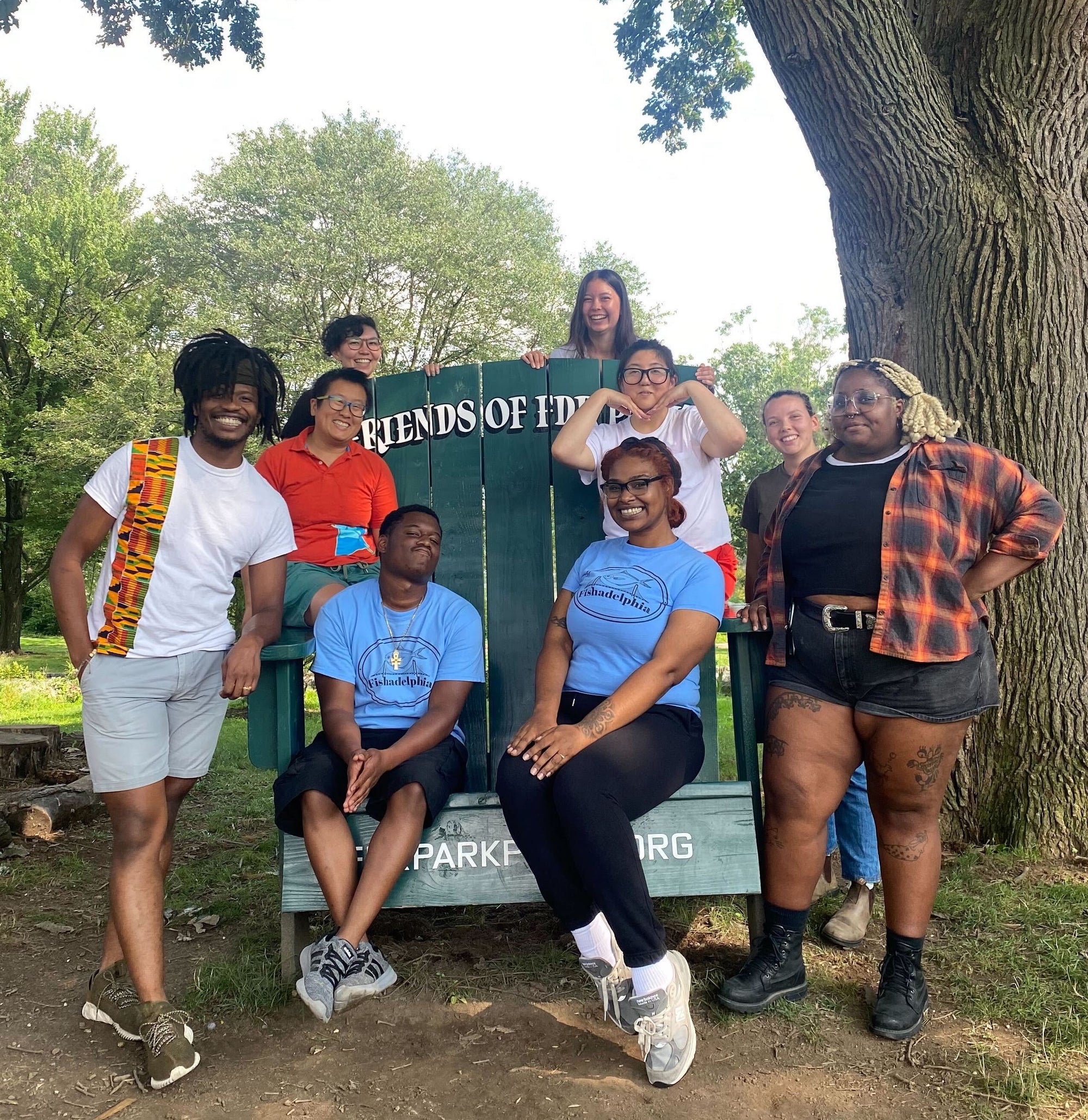 Fishadelphia staff, all of whom are POC sit and stand by an oversize chair at FDR park