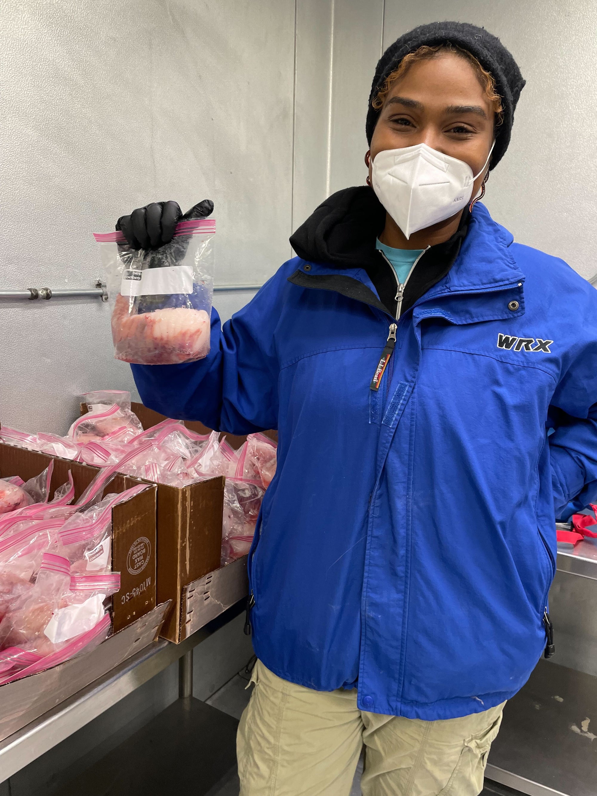 Tasha, Director of Seafood Management, smiles while wearing a mask and holding a share of seafood in a cold room.